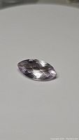 Close-up photo of a marquis checkerboard cut pink amethyst gemstone showing facets and color on a white background.