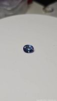 Loose oval cut natural blue tanzanite gemstone displayed on white surface, showing facets and color