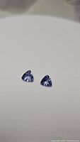 Close-up photo of two natural trillion cut tanzanite gemstones set on a neutral background, showing clarity and color.
