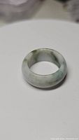 Solid jade ring showing natural mottled green patterns from Myanmar jade, polished rounded shape on white background.