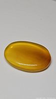 Close-up photo of a large, bright yellow natural onyx oval cabochon gemstone on a white background showing smooth polished dome and rich color.