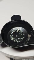 Small loose round-cut alexandrite gemstones in a black dish under bright white light showing their natural appearance and color.
