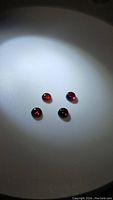 Photo of four round cabochon rhodolite garnet gemstones in shades of purple-red, on white background under focused light.