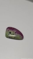 Polished ruby zoisite cabochon gemstone showing vibrant red and green colors with black markings.