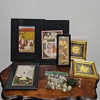 Full overview of framed art prints, two gold framed sun motif pieces, and bag of assorted decorative small items on wooden table.