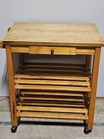 Front view of the wooden butcher block cart showing the two slatted shelves and drawer.