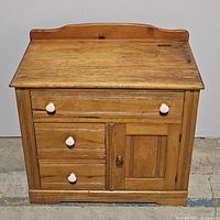 Front view of wooden cabinet showing three drawers and single door. Cabinet has white round drawer knobs and brown round door knob. Top surface has backboard edge.