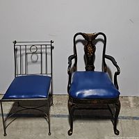 Two chairs shown side-by-side against a plain background: one metal frame chair with blue vinyl cushion, one wooden armchair with decorative carved details and blue vinyl cushion.