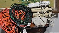 Overview of assorted extension cords and surge protectors piled on small table with floral background