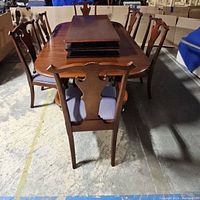 Full view of dining table with six chairs placed around it and two table leaves stacked on top.