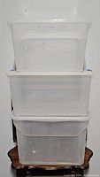 Three clear plastic storage bins stacked on a small wooden table, showing overall shape and size.