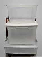 Stack of three translucent plastic bins with white lids, showing the bins from front angle, stacked one on top of the other.