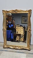 Full front view of the large rectangular mirror showing the reflective surface and gold ornamental plastic frame with floral and scroll detailing.