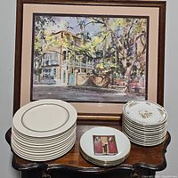 Photo showing three stacks of plates in front of framed picture, clear view of dinner, salad, and decorative plates