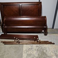Full view of disassembled king size sleigh bed parts including headboard, footboard, and side rails laid out on concrete floor