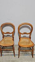 Pair of vintage wooden chairs with rattan seats and curved carved backs, shown from front