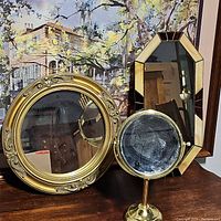 Photo showing the set of three vintage mirrors: octagonal wall mirror with beige and brown beveled glass border, round wall mirror with ornate gold frame, and small round table mirror on brass stand.