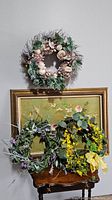 Three spring floral wreaths displayed on a wall above a small wooden table with a framed artwork behind