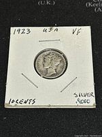 Front side of 1923 US Silver Mercury Dime with Mercury Head design held in a white paper coin holder with handwritten notes.
