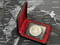 Silver coin in protective case with red lining resting on a map background.