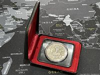 Closed display case showing the silver coin inside, with red velvet lining around the coin holder.