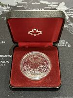 Specimen silver dollar coin in red presentation box showcasing maple leaf inside lid.