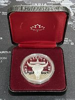 The coin inside a black presentation case with red velvet lining, showing the maple leaf emblem inside the lid.