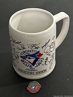 Photo showing white ceramic mug with Toronto Blue Jays 1985 Champions logo and player autograph prints around it.