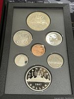 Top view of seven Canadian proof coins in a black display case including the double dollar coin and commemorative 1867-1987 coin.