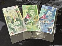 Front side of three Eastern Caribbean banknotes: two $5 notes and one $10 note displayed in plastic sleeves on a dark map background.