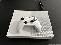 Top view of white Xbox One S console with white wireless controller placed on top and power cord in background
