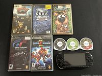 Overview of gaming system with 5 game cases and 3 UMD discs, all arranged on a black surface.