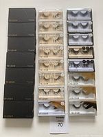 Photo of 23 pairs of Velour brand false lashes from various collections. Displayed in both black boxes and clear cases showing different lash styles and packaging.