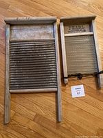 Photo shows two antique wooden washboards. The larger has a metal ridged washing surface, the smaller has a broken glass ridged surface held with wire, branded Pearl.