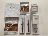 Top-down view of complete Bella Lash eyelash extension system with adhesive, cleaning powder, two tweezers, adhesive wipes container, TapeX tape and scissors pouch