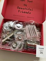 Top view of the open red box with multiple packaged false lashes, lash adhesive pens, and transparent lash cases inside.