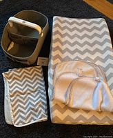 Photo showing a Skip Hop diaper caddy, gray and white chevron large change pad, a smaller matching change mat, and three beige Munchkin change pads