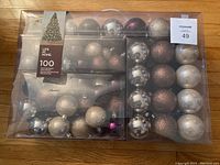 Photo of sealed package containing 100 shatterproof Christmas ball ornaments in various colors and finishes including silver, gold, bronze, and pearl white.