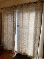 Curtain panels hanging on a window allowing light to filter through, showing the grey geometric pattern on an off-white background.