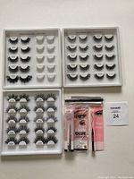 Three trays containing a variety of false eyelashes and three different adhesive eyeliners placed in front of the trays, all brand new and unopened.