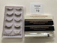 Set of five pairs of false eyelashes, lash adhesive eyeliner pens in black and white packaging, and white makeup remover pen in plastic sleeve.
