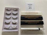 Photo of set showing five pairs of false lashes in clear packaging with labels, three boxes of lash adhesive eyeliner kits in black and white, and one makeup remover pen in plastic wrapper.