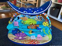 Full view of the Finding Nemo themed baby tummy time mat with ocean characters and blue manta ray arch with multiple hanging toys.