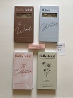 Four boxed sets of FlutterHabit false lashes and one box of Made For This lash adhesive arranged flat showing front packaging.