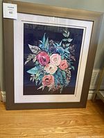 Framed floral artwork with a bouquet of pink, white and orange roses surrounded by green and blue leaves in a wide taupe frame with a white double mat border.
