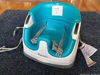 Front angle view of turquoise seat insert with safety harness straps attached to white plastic booster seat base.