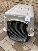 Front view of the large beige plastic dog crate with metal wire door, placed on stone tile floor outside.