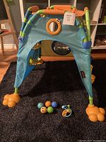 Front view of Yookidoo toddler play tent standing on carpet, with 5 colorful balls and keys placed in front.
