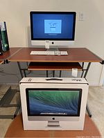 iMac on wooden desk with wired Apple keyboard positioned in front and original retail box on floor.