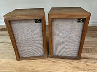 Front view of two Audio Dynamics bookshelf speakers with wood veneer and beige fabric grilles.